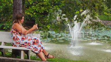 金发女郎坐在公园内的喷泉触摸式电话台<strong>上</strong>